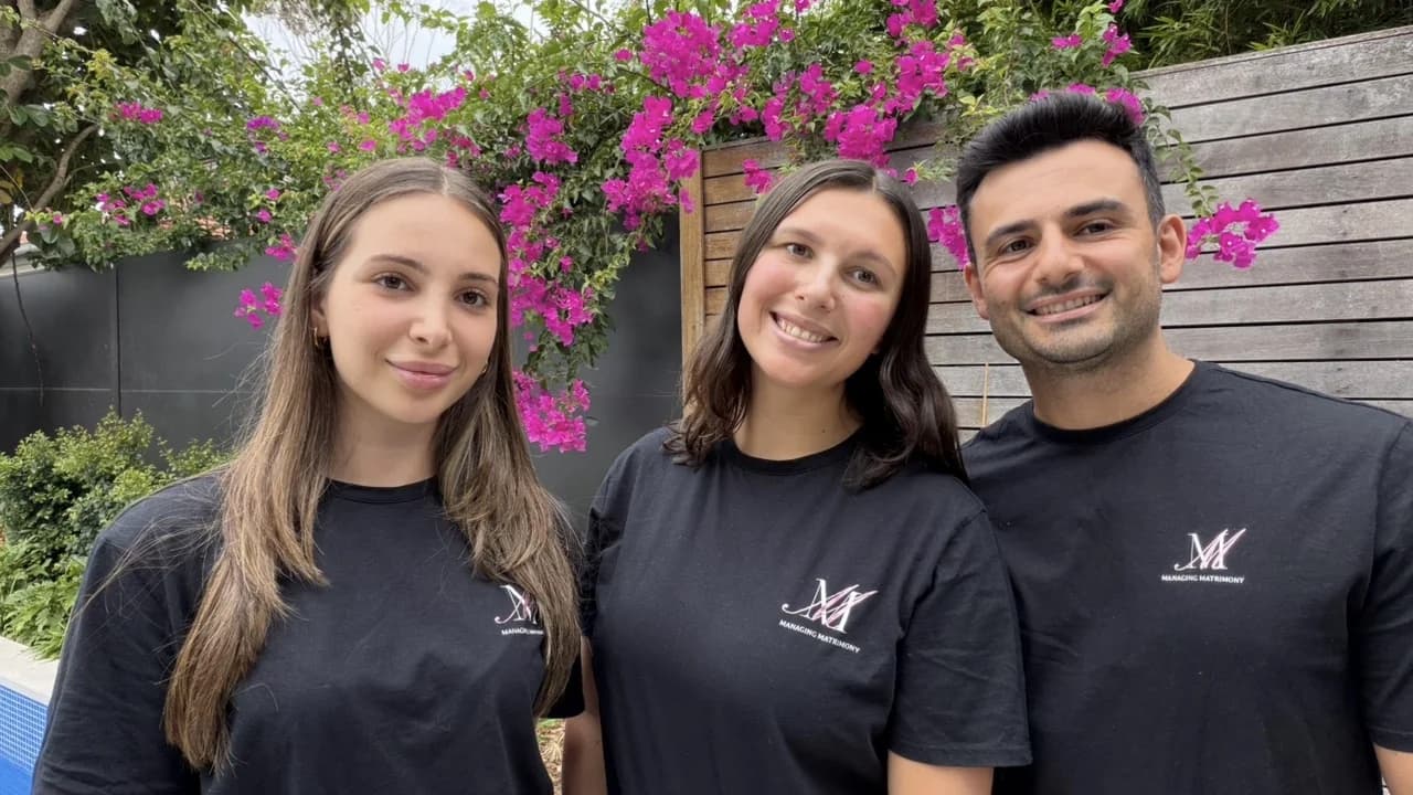 Jordan, Michael and Bella of Managing Matrimony, smiling together under a flowering bougainvillea