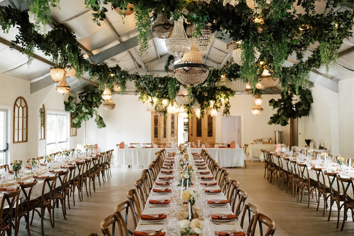 Long tables set for dinner under greenery and chandeliers, at Jordan and Michael's own wedding at The Woods Farm, Jervis Bay