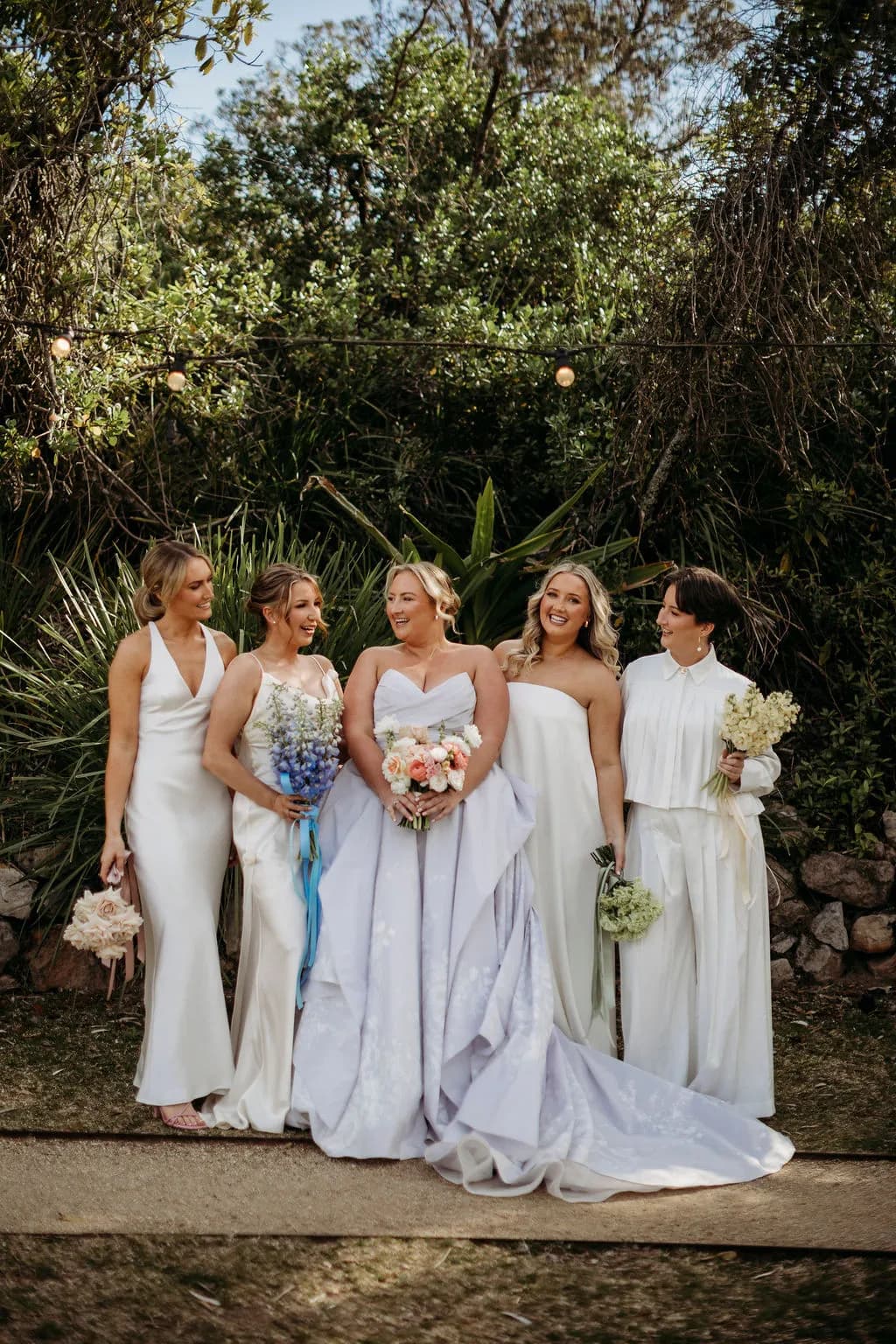 Bride with bridesmaids holding bouquets in a garden setting at The Cove Jervis Bay, relaxed coastal wedding style
